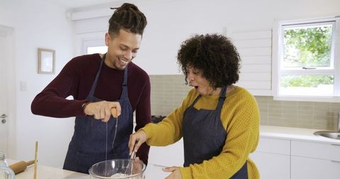African american couple cooking together cracking egg and whisking in bright home kitchen