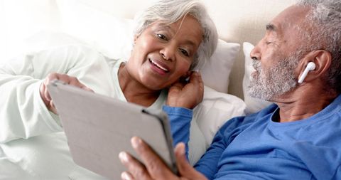 Senior Couple Using Tablet and Sharing Earphones in Bedroom