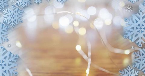 Twinkling warm fairy lights over wooden table with blue snowflake holiday background