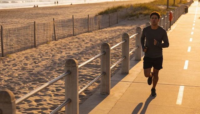 Solo morning beach runner jogging along sunlit coastal promenade during golden hour