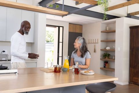 Senior black man and white woman chatting and enjoying breakfast at sunlit kitchen island