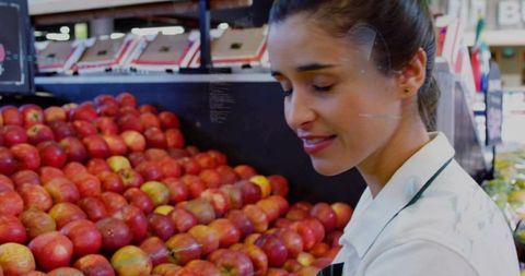 Young supermarket produce clerk stacking red apples on retail display