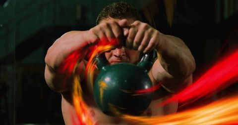 Kettlebell power swing with red-orange light trails featuring muscular shirtless athlete