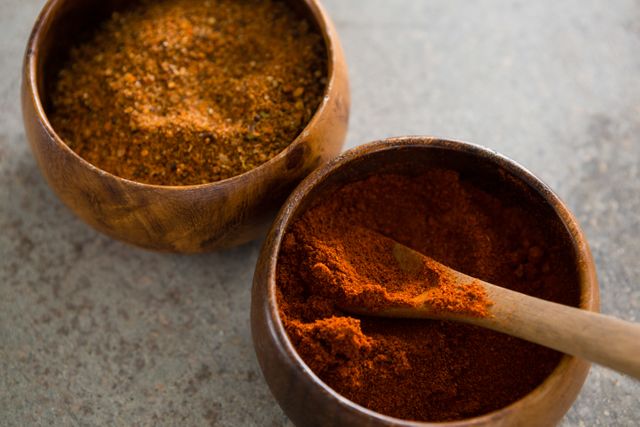 This image shows a close-up view of cinnamon powder and red chili powder in wooden bowls. Ideal for use in culinary blogs, recipe websites, cooking magazines, and food-related advertisements. Perfect for illustrating articles on spices, seasoning, and natural cooking ingredients.