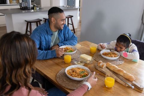 Family enjoying spaghetti at kitchen table with bread and orange juice