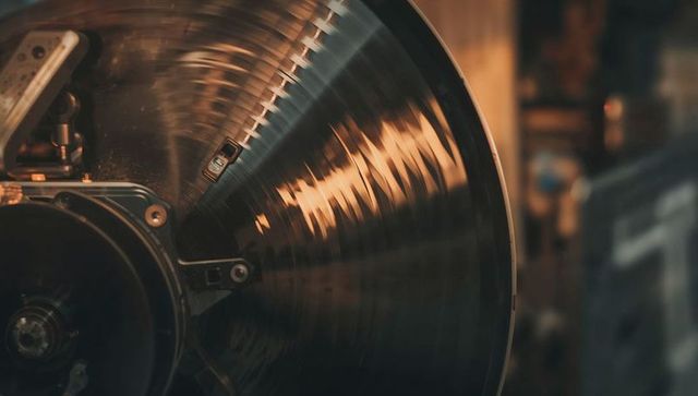 Spinning grooved metal disc reflecting warm workshop light with visible cartridge arm