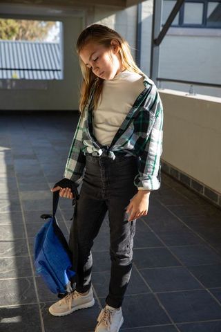 Young girl with backpack standing in sunlit school corridor
