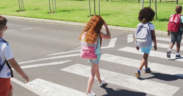 Children are crossing a street on a marked crosswalk with backpacks. The scene emphasizes pedestrian safety and highlights the active back-to-school period. Useful for educational materials, articles on child safety, and back-to-school promotions.