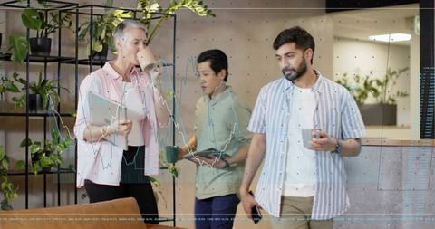 Casual office team chatting and sipping coffee in modern lounge with plants and devices