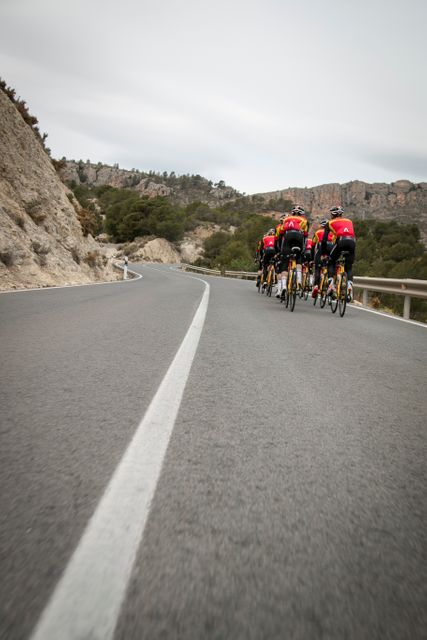 Group of cyclists riding on a mountain road, training together in a scenic outdoor environment. Perfect for advertising sports events, fitness programs, or promoting tourism in mountainous regions. Ideal for illustrating concepts of teamwork, endurance, and outdoor activities.