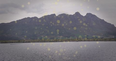 Undulating mountain ridge over calm lake with golden bokeh light reflections