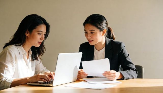 Asian businesswomen collaborating over laptop and documents during office meeting