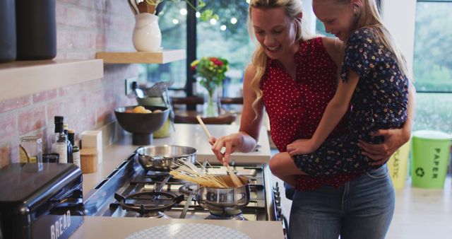 Happy caucasian mother holding daughter and preparing food in kitchen. Cooking, family, domestic life and togetherness.