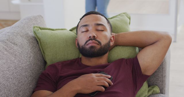 Tired biracial man with dark beard sleeping on sofa at home. Relaxation, family, lifestyle, domestic life, unaltered.