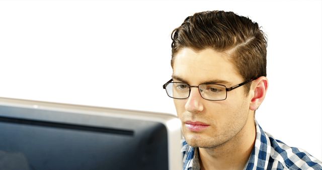 Young man with glasses and plaid shirt working intently on computer. Ideal for illustrating concepts related to technology, office work, professionalism, and concentration.