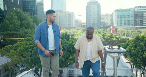 Two men walking up city stairs holding smartphone and talking over urban green canopy