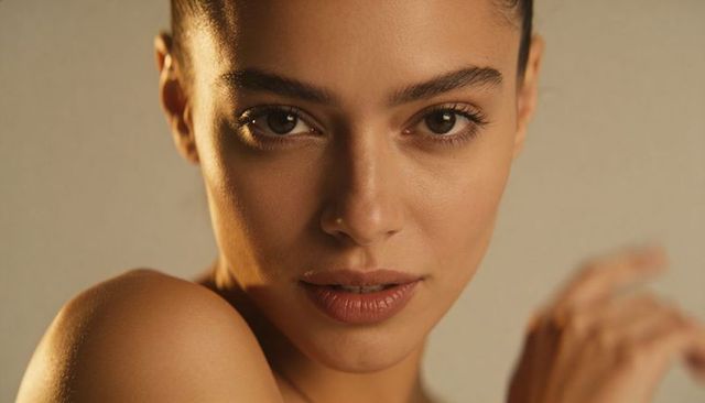 Woman holding direct gaze in warm studio closeup with bare shoulder and soft lighting
