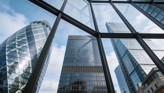 Glass atrium framing gherkin and modern skyscrapers reflecting blue sky over london skyline