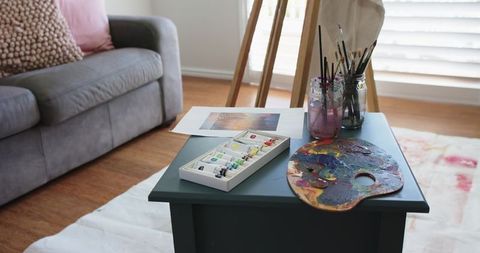 Artist workspace featuring paint palette, tubes and brushes on dark teal side table