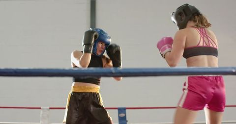 Female Boxers Sparring in Ring Wearing Headgear and Gloves During Intense Training Session