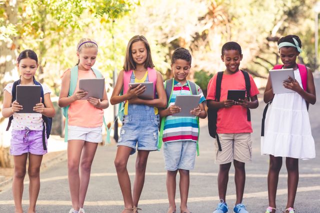 Group of diverse school children using digital tablets while walking outdoors. Ideal for educational content, technology in education, back-to-school promotions, and articles on digital learning and childhood development.