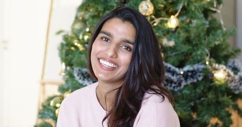 Cheerful Indian Woman Smiling by Christmas Tree at Home