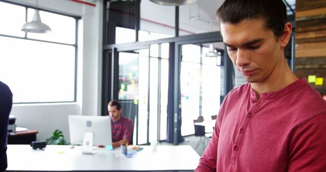 Young Man Working in Modern Office with Colleague in Background - Download Free Stock Images Pikwizard.com