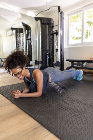 Focused african american woman planking on exercise mat in fitness room