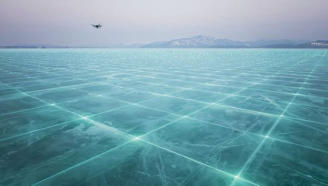 Hovering drone mapping frozen turquoise lake with glowing grid and distant mountains