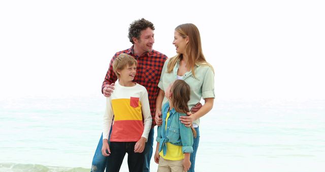 Family standing on the beach, enjoying their time together. Parents smiling and interacting with their two children. Could be used for ads promoting family vacations, travel destinations, and outdoor activities.