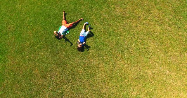 Two children relaxing on green grass on a sunny summer day. Great for advertisements, blogs, and articles related to outdoor activities, childhood, nature, and leisure. Ideal for use in campaigns promoting summer events, playtime, and carefree moments.