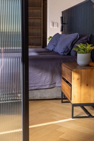 Minimal modern bedroom with dark gray bedding, wooden nightstand and sunlit ribbed glass