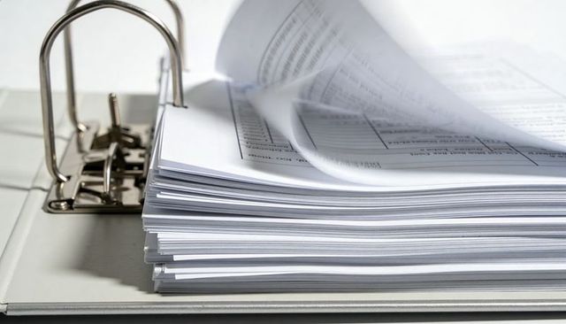 Thick stack of printed forms with one page flipping in two-ring metal binder