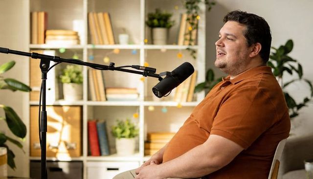 Male podcaster recording at home studio with broadcast microphone and bookshelf backdrop