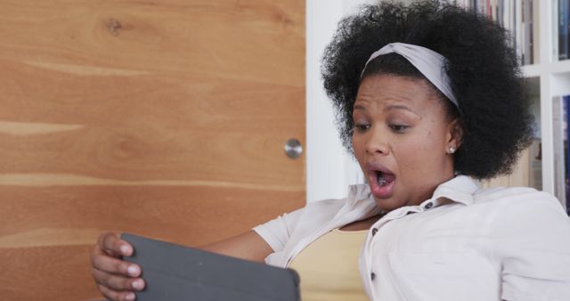 Shocked biracial plus size woman using tablet at home. Domestic life, technology, communication and lifestyle, unaltered.