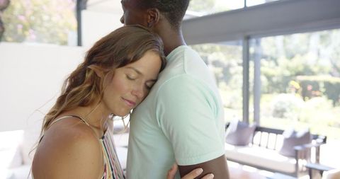 Diverse couple embracing at home in sunlit living room