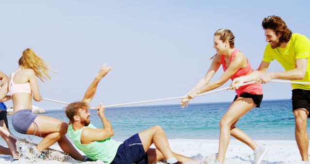 Group of young active friends playing tug-of-war on a sunny beach. Perfect for promoting outdoor activities, summer vacation spots, team-building exercises, and friendly competition. Captures fun and active lifestyle with a scenic coastal backdrop.