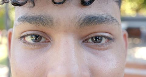 Closeup male headshot showing focused eyes and skin texture in warm park light