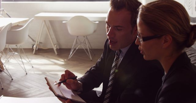 Caucasian Businessman and Businesswoman Discussing Notebook in Bright Office Setting - Download Free Stock Images Pikwizard.com