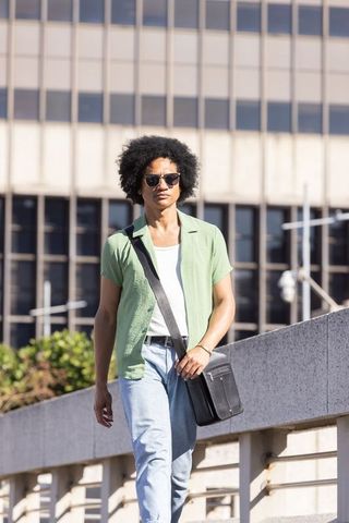 African american commuter walking with satchel wearing sunglasses near office building