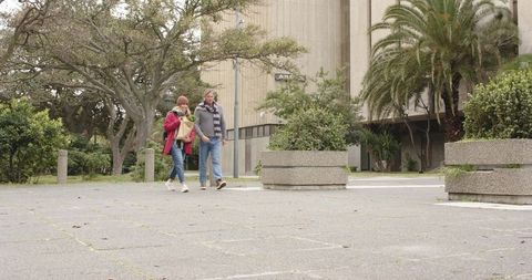 Mature couple walking through urban courtyard with concrete planters and palm trees