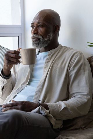 Senior african man sipping coffee by sunny window, gazing contemplatively