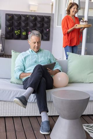 Senior couple enjoying patio celebration with man using tablet and woman carrying cake