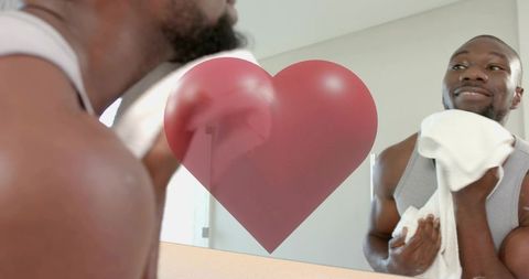 Man drying face at mirror with red heart decal, smiling during morning self-care routine