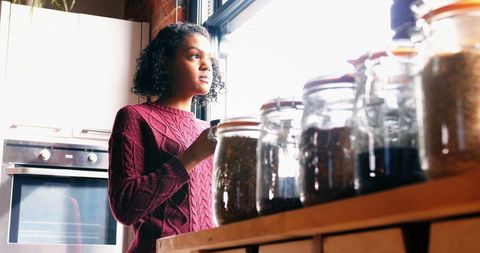 Reflective Woman Holding Coffee by Kitchen Window
