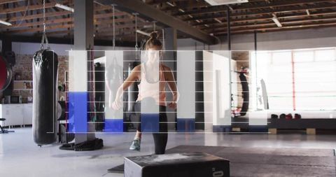 Athletic woman balancing on plyo box during plyometric workout in industrial gym loft
