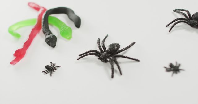 Black spiders and colorful toy snakes are scattered over white background. Perfect for use in Halloween promotions, children's party decorations, or educational material about insects and reptiles. Ideal for various craft projects or as spooky elements in event planning.