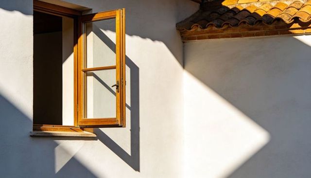Sunlit Open Wooden Casement Window Casting Geometric Shadows on White Plaster Facade