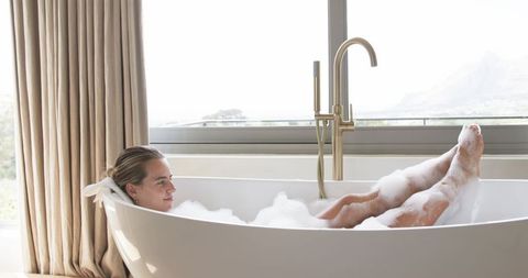 Woman relaxing in bubble bath with mountain view and brass freestanding faucet