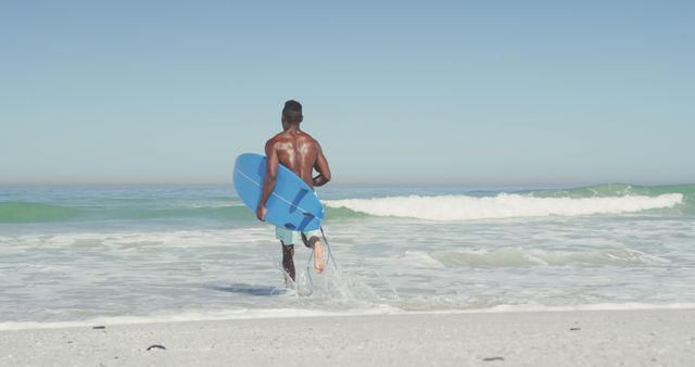 African american man running on sea and holding surfboard. Summer, relaxation, vacation, happy time, summer time.